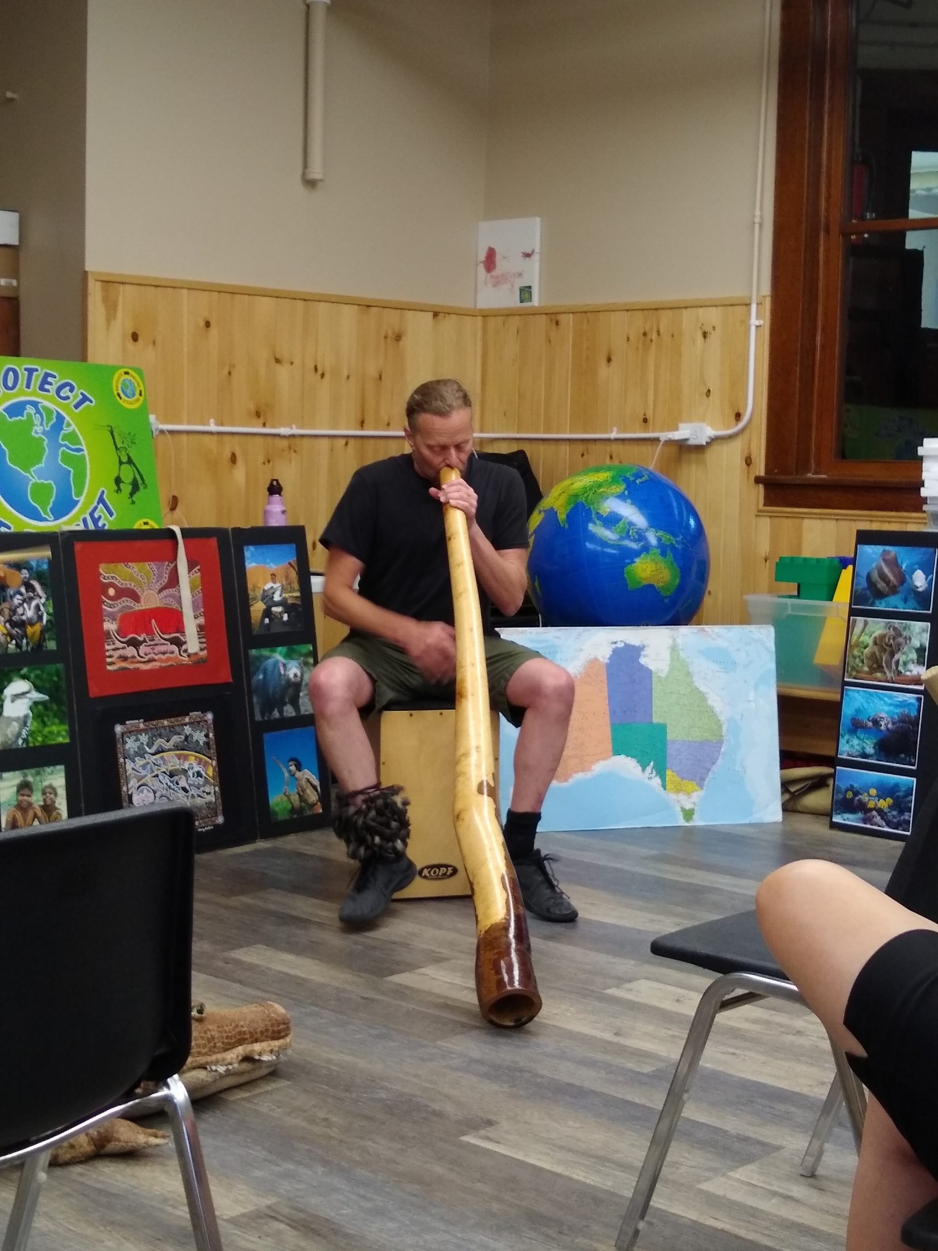 A man plays a didgeridoo and a cajon or a box drum at the same time