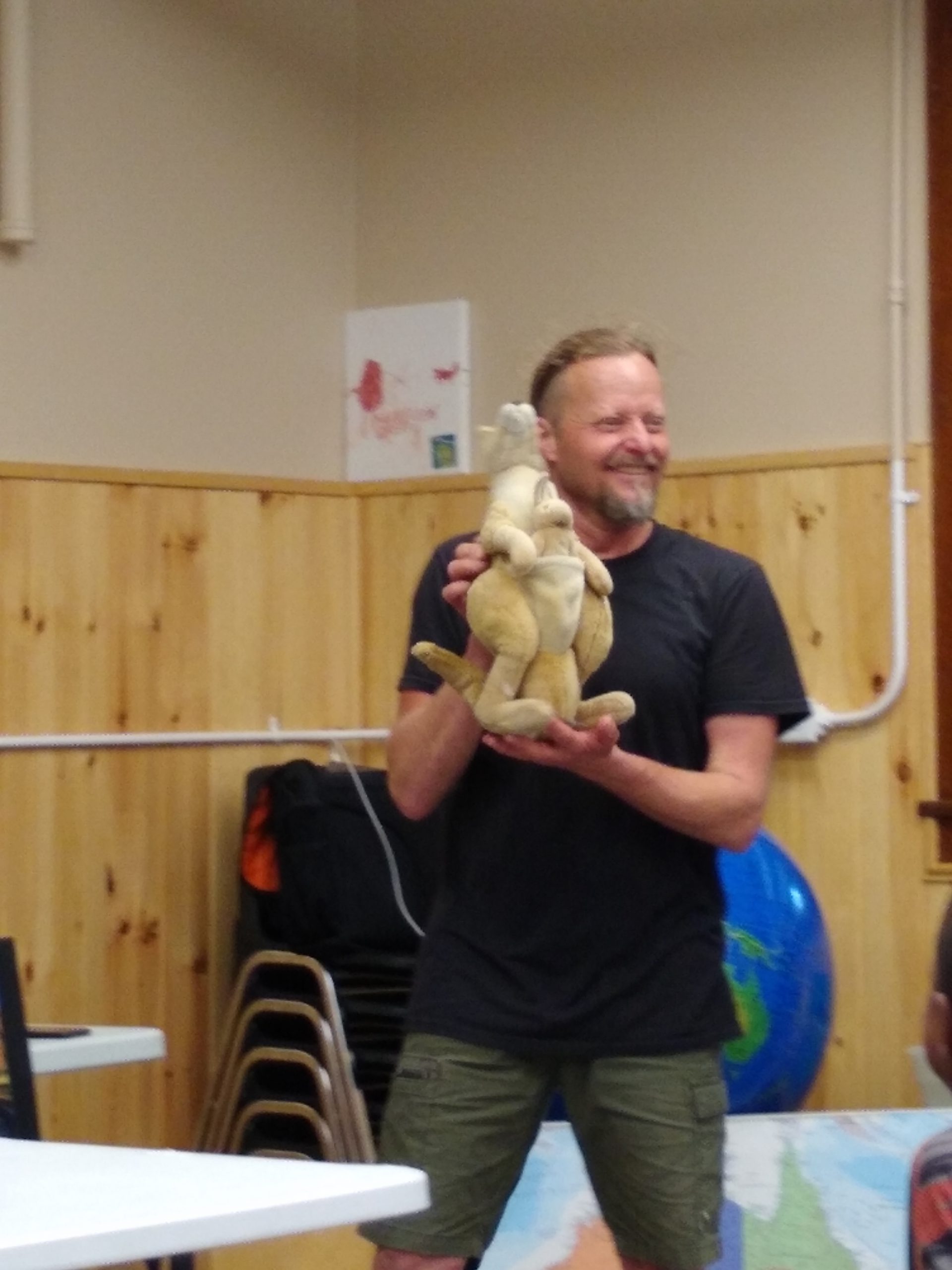 A man holds a stuffed kangaroo and joey toy and smiles as he talks about Australian animals